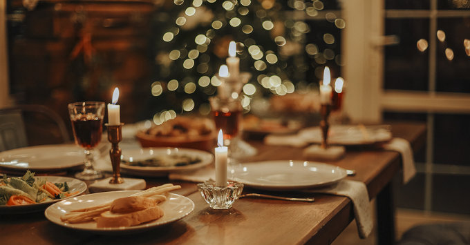 holiday table setting with christmas tree/lights in background and lit candles in foreground
